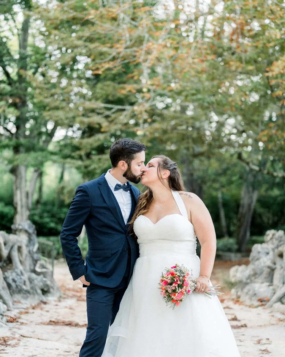 Bride and groom kissing on a park path, colourful bouquet in hand
