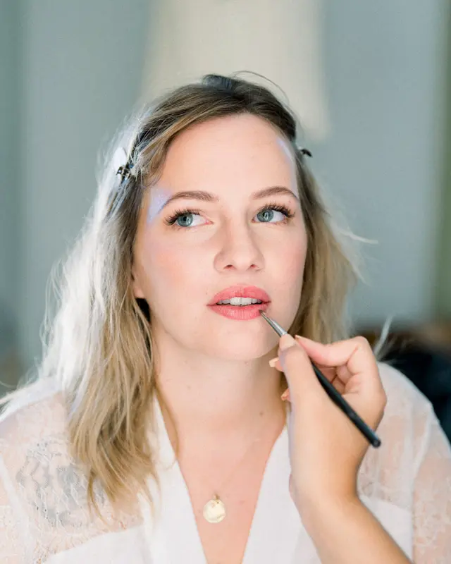 Makeup artist applying the bride's lipstick while she gets ready