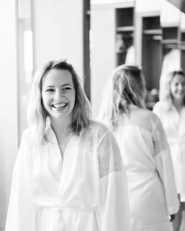 Smiling bride in a white robe with her friends getting ready, in black and white