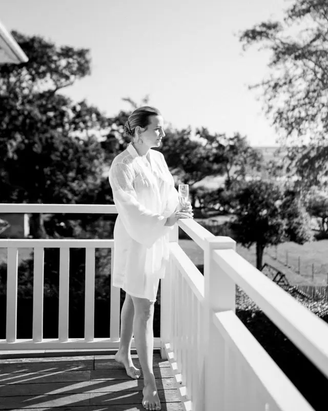 Bride in a robe on the villa's terrace looking out over the bay, black and white