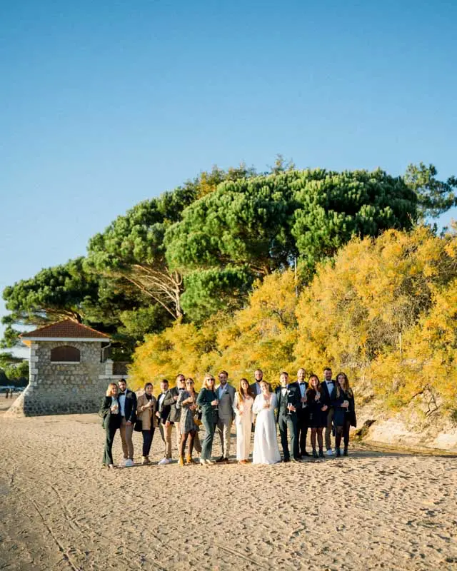Group photo of the couple and guests on the beach beneath the pines