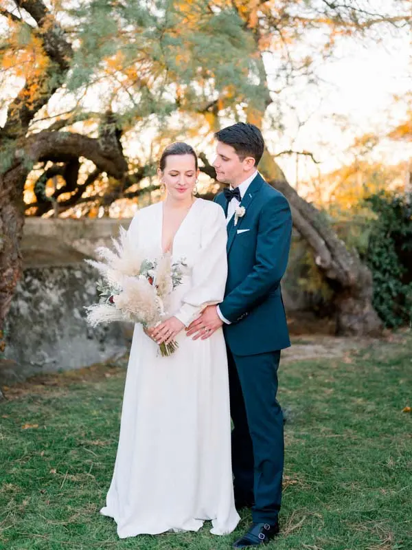 Couple embracing beneath a golden tree in late afternoon, pampas bouquet in hand