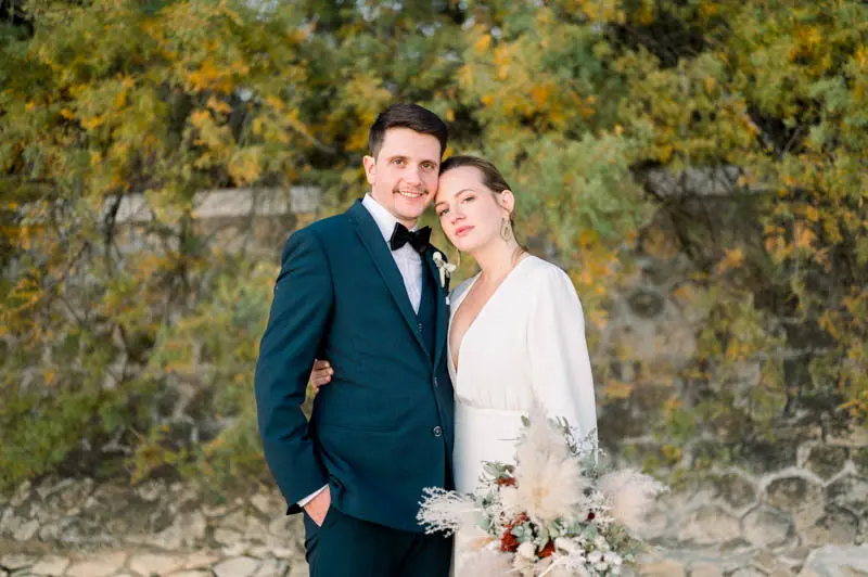 Smiling bride and groom in front of golden shrubs by the bay