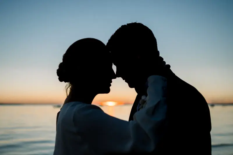 Silhouettes of the couple forehead to forehead at sunset over the bay