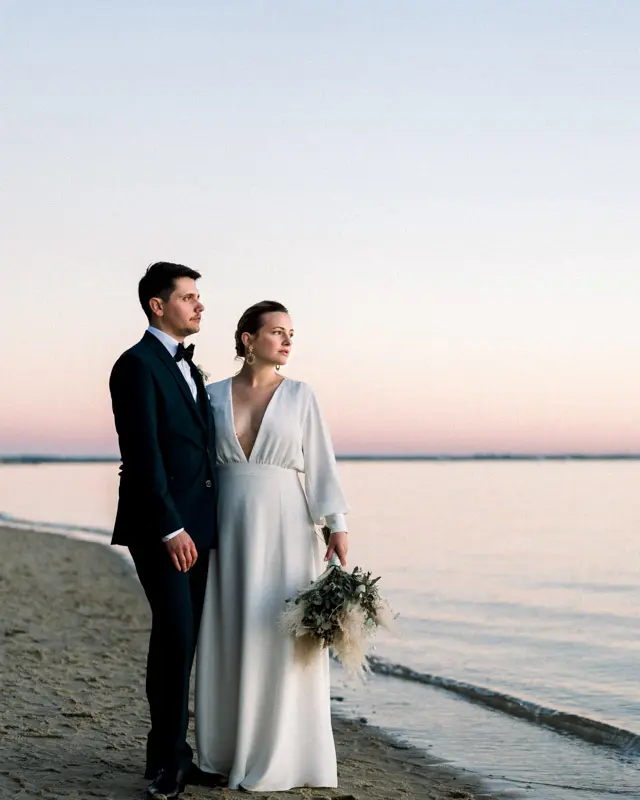 Bride and groom at the water's edge on an Arcachon Bay beach at dusk