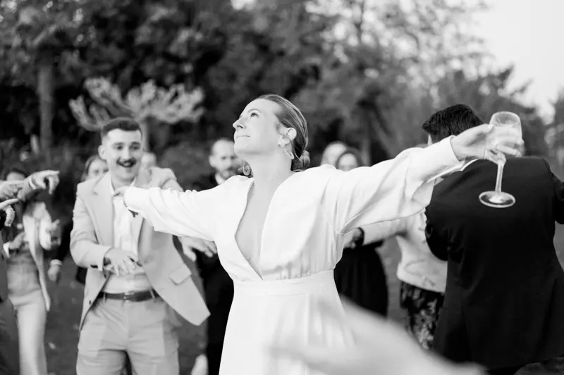 Bride dancing joyfully with open arms among her guests, black and white