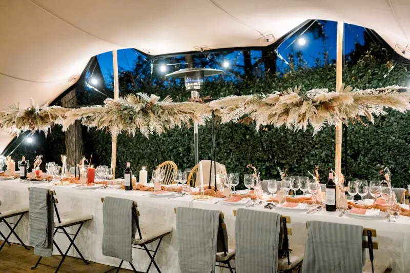 Long reception tables under the tent with pampas garlands and string lights