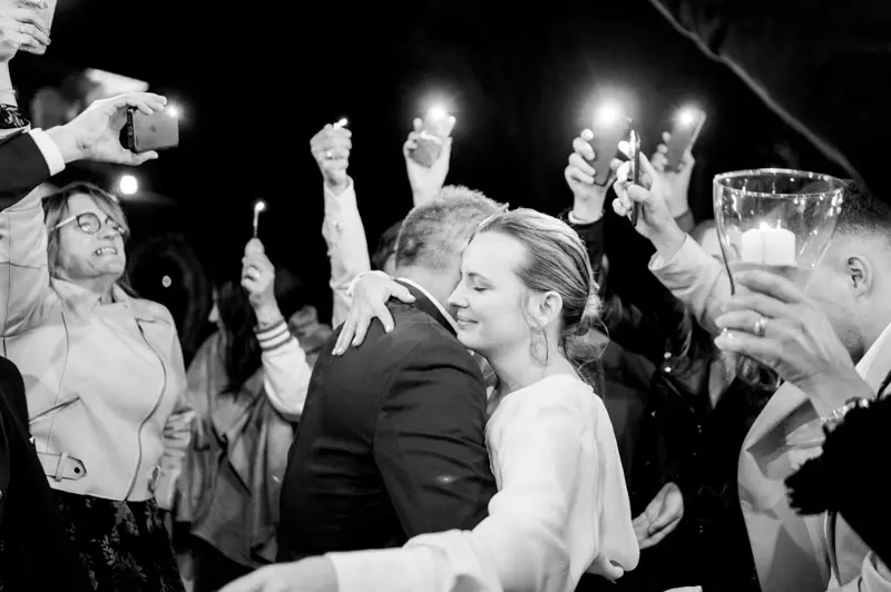 Couple surrounded by guests waving sparklers, in black and white