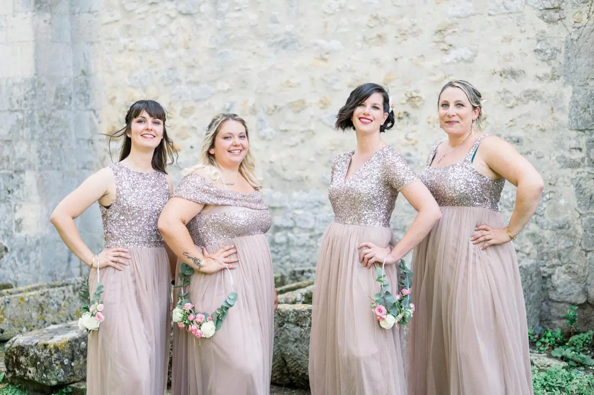 Bridesmaids in nude sequinned dresses posing against a stone wall