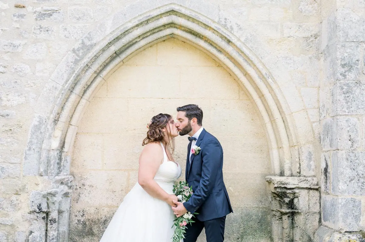 Bride and groom kissing beneath a Gothic stone arch at Domaine de Cordet