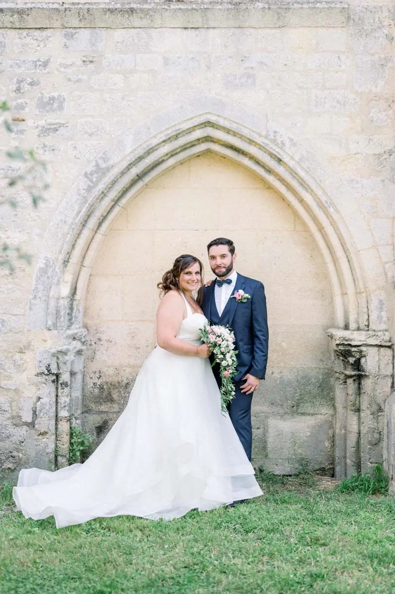 Bride and groom posing in front of a Gothic stone arch on the grass