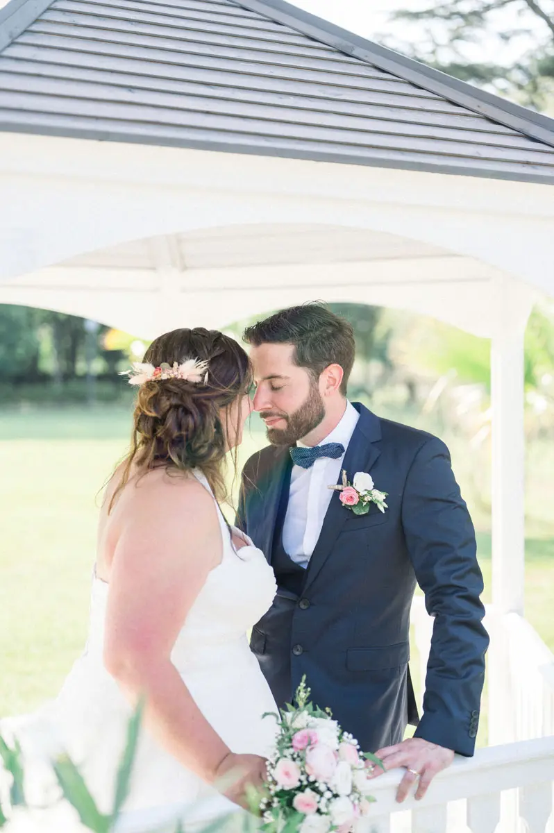 Bride and groom gazing at each other under the white gazebo, bouquet in hand
