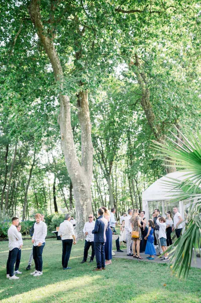 Guests gathered in the shade of tall trees for the drinks reception