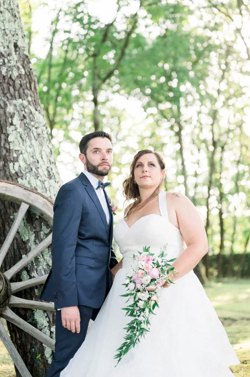 Bride and groom posing by a tree beside a wooden wheel at Domaine de Cordet