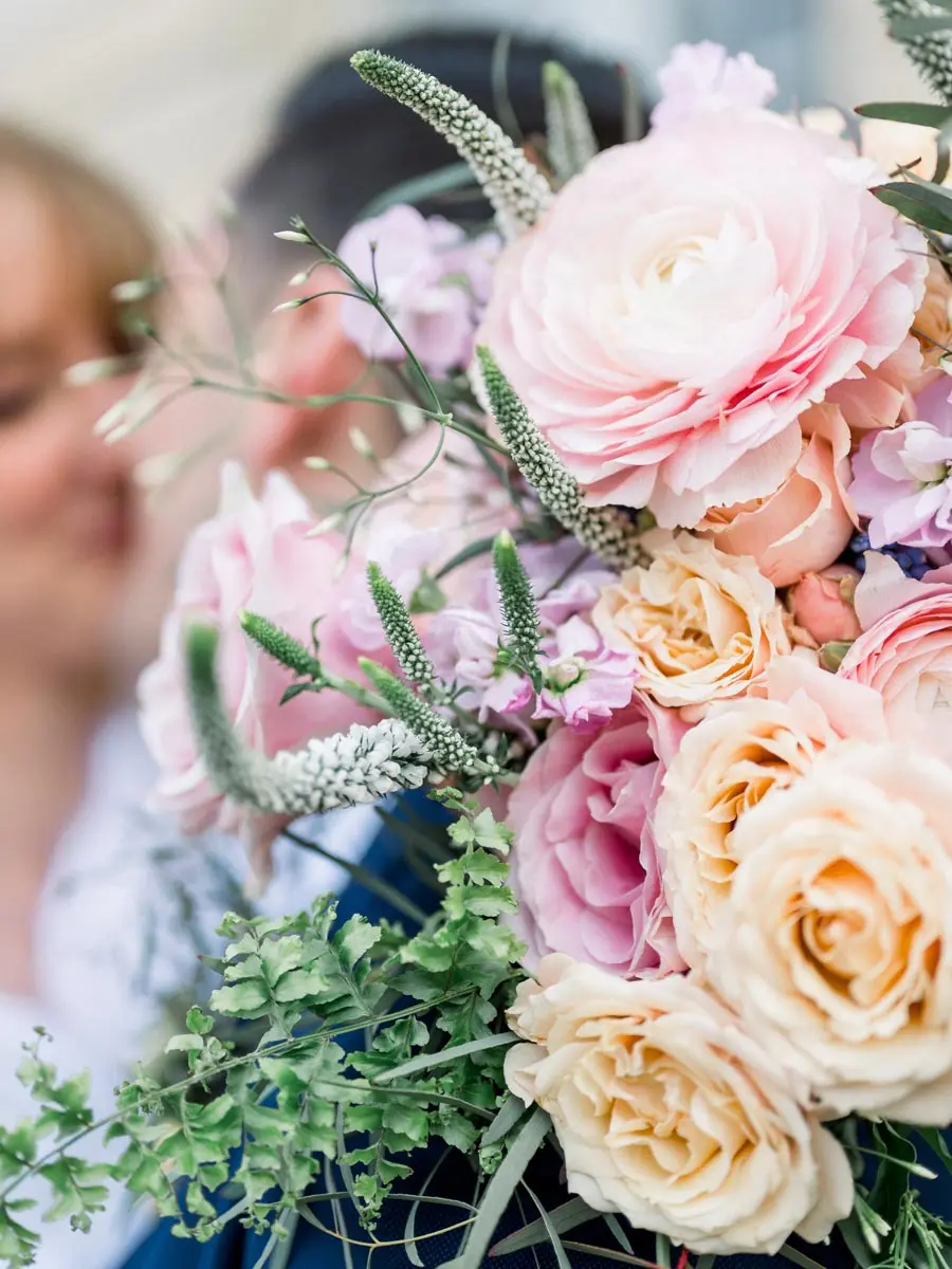 Bouquet of peach roses and pink ranunculus in front of the couple's kiss
