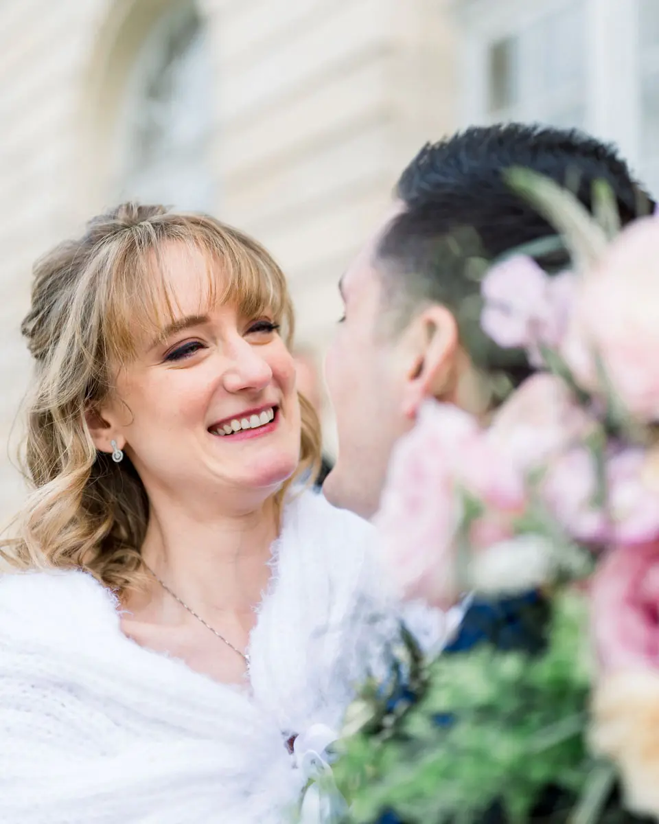 The laughing bride cheek to cheek with the groom, pastel bouquet in the foreground