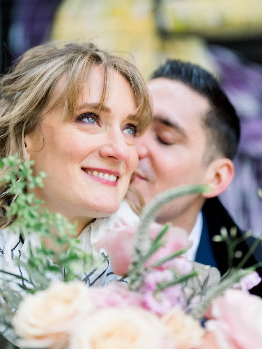 The smiling bride nestled against the groom with a pastel bouquet