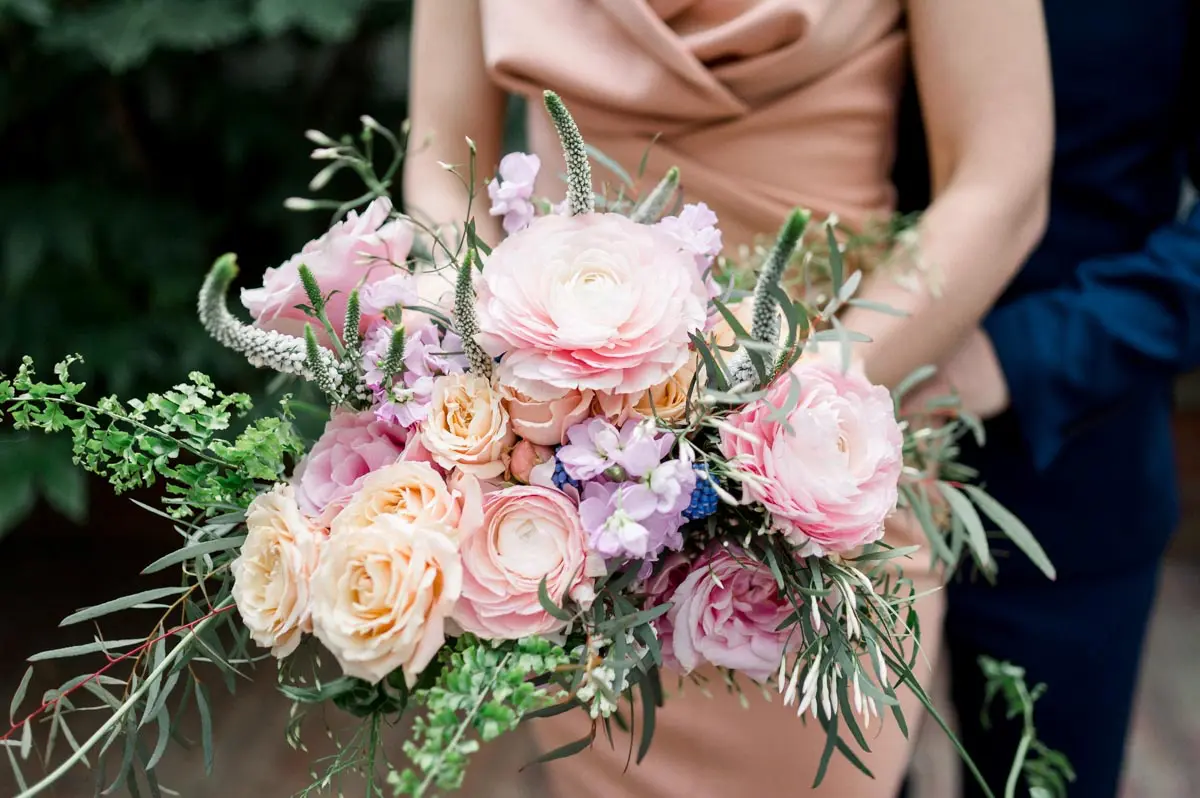 Pastel bouquet of roses and ranunculus held against the bride's pink dress