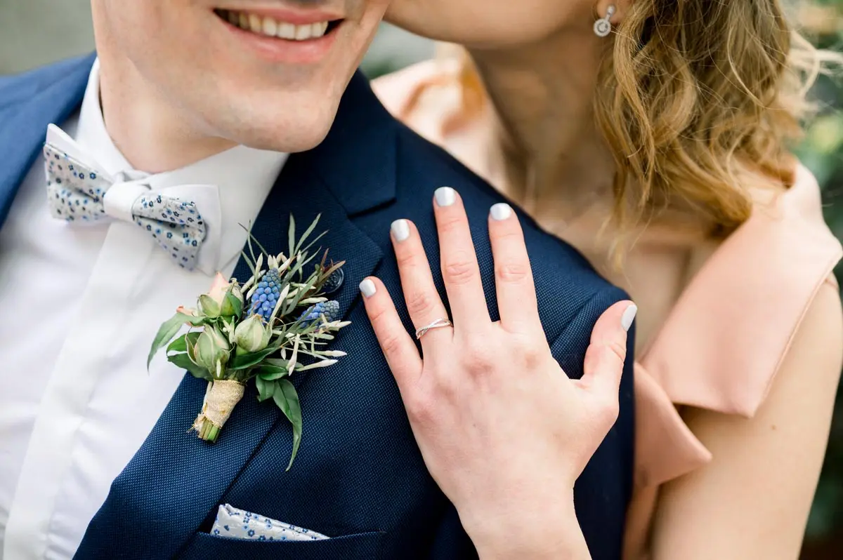 The bride's hand and wedding ring resting on the groom's blue jacket