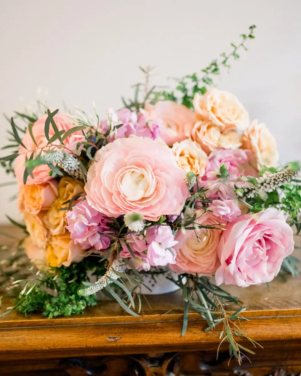 Bouquet of pink and peach roses and ranunculus on a wooden sideboard