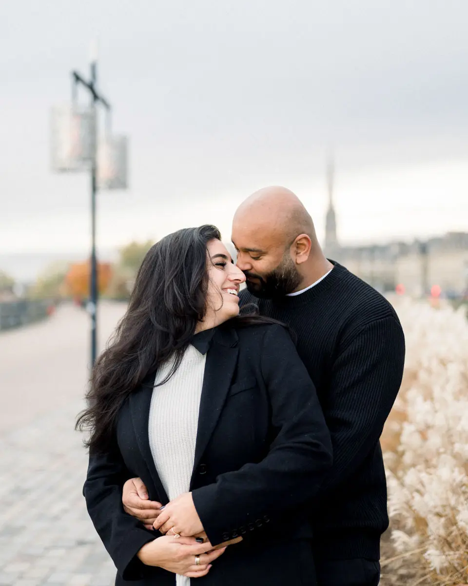 He kisses his smiling fiancée's forehead on the Bordeaux quays