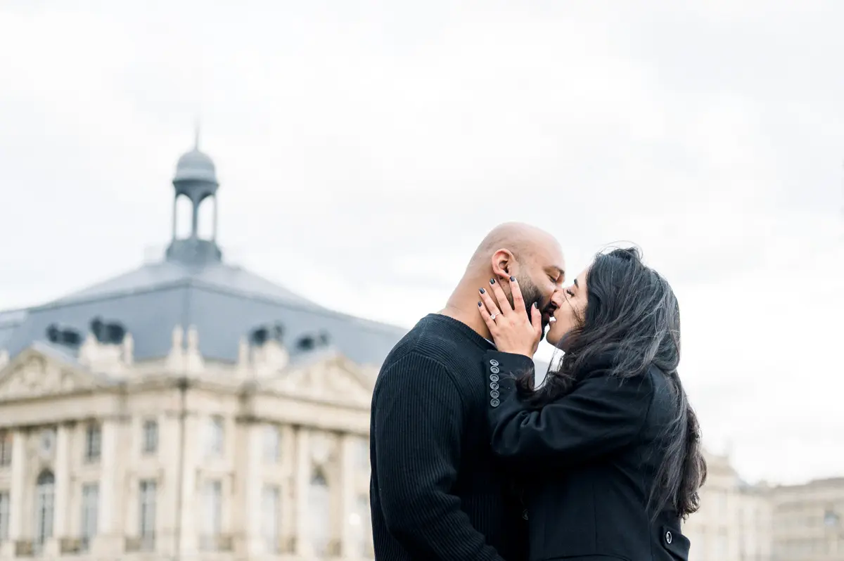 Engaged couple kissing before the rooftops of Place de la Bourse, Bordeaux