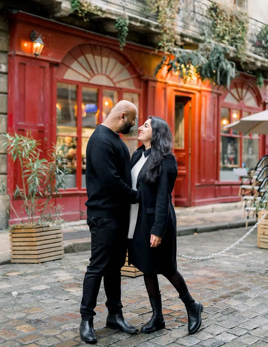 Engaged couple gazing at each other before a red shopfront in old Bordeaux
