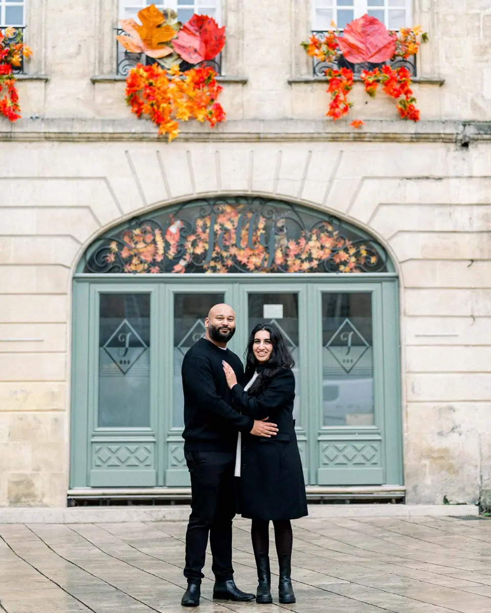 Engaged couple embracing before a sage-green door under floral decorations