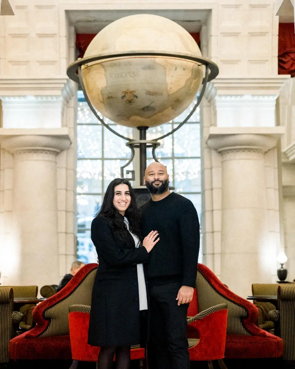 Engaged couple embracing beneath a large globe in the Grand Hôtel lobby