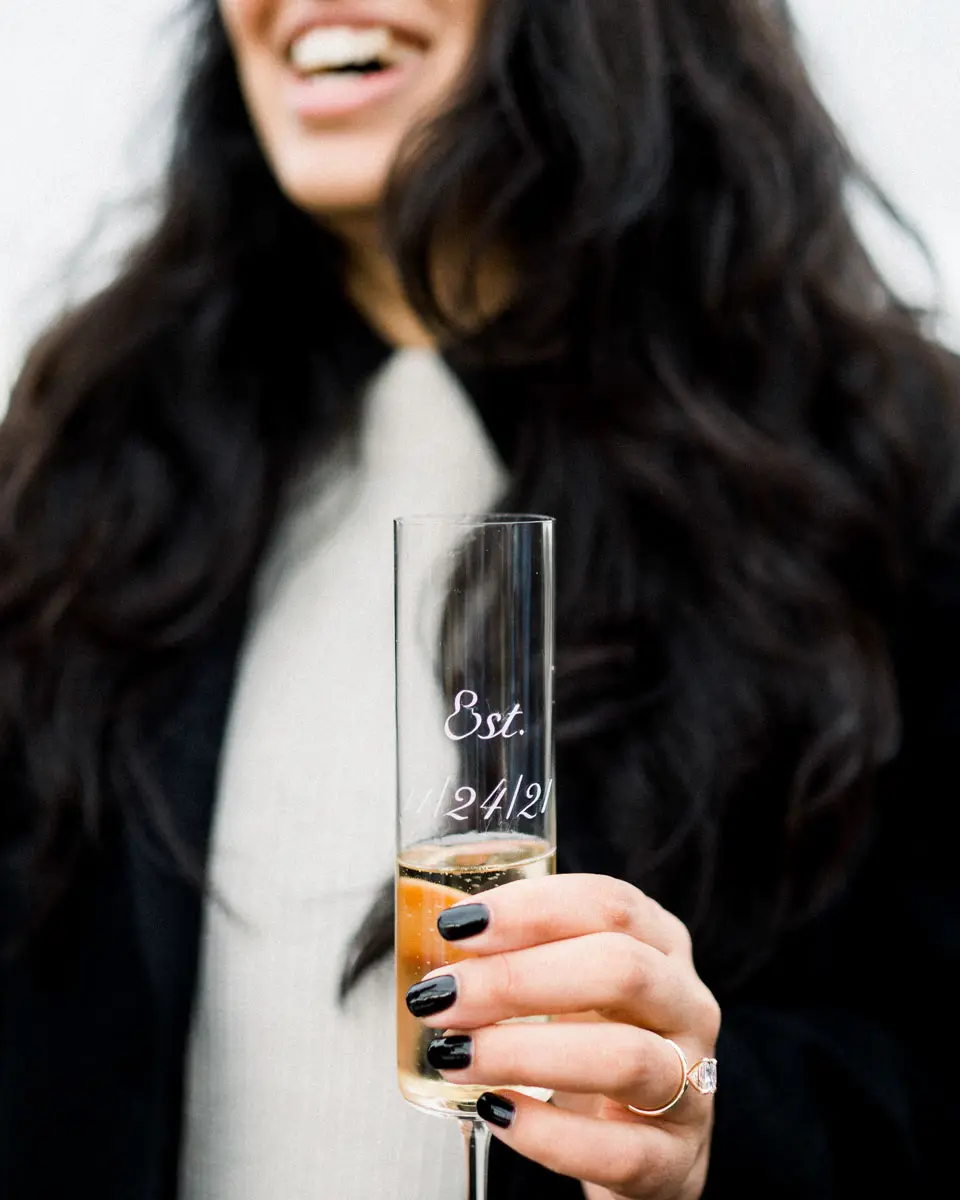Nisha laughing with an engraved champagne flute and ring on her finger