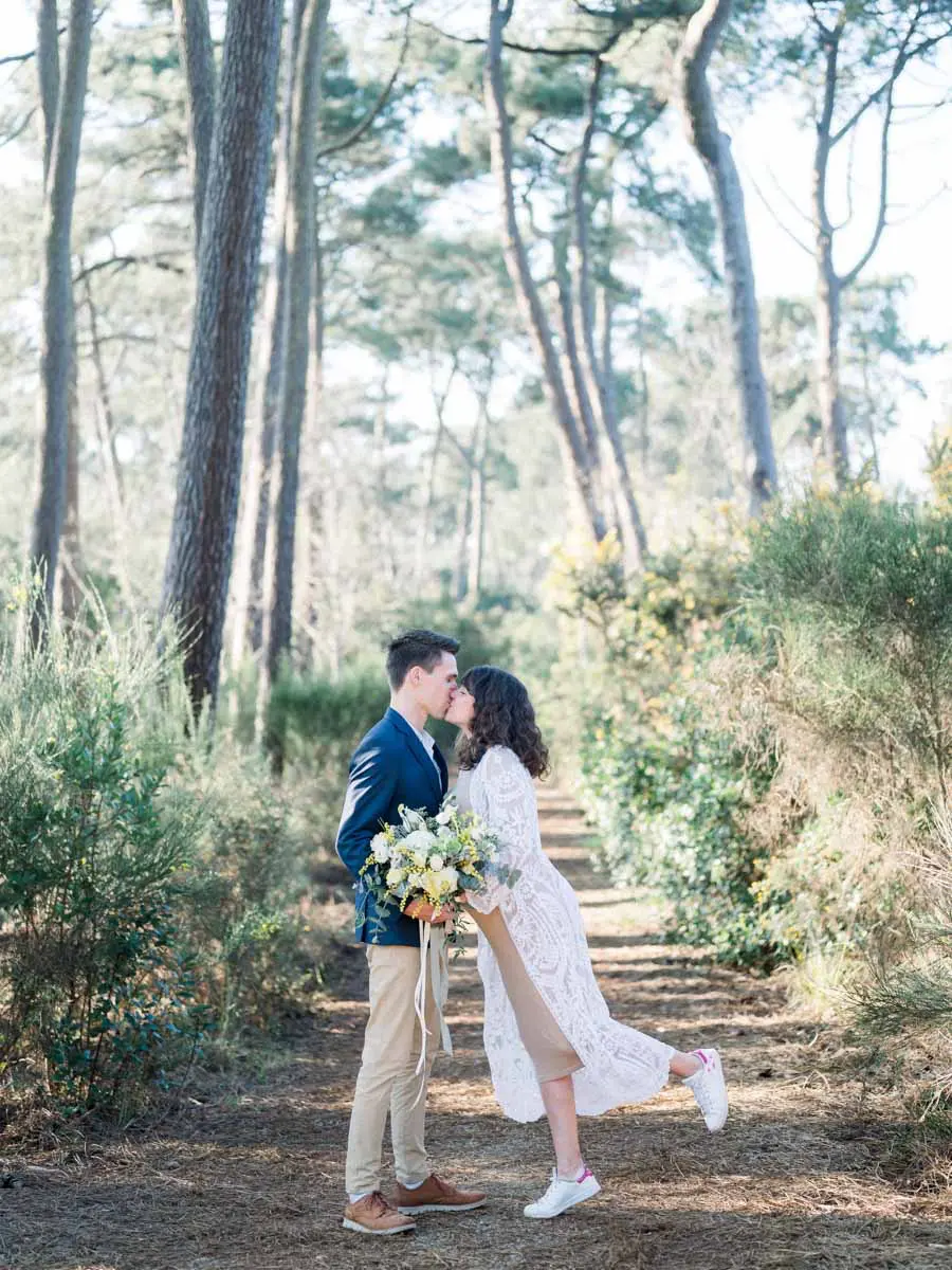Couple kissing on a path beneath the pines, bouquet in hand