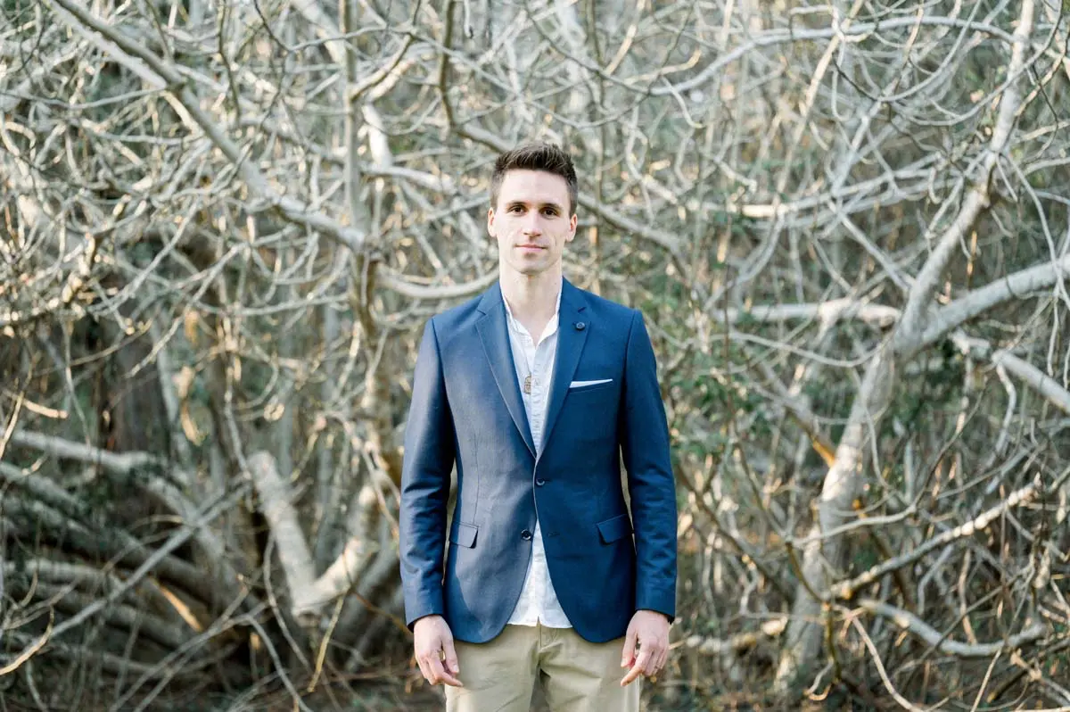 Father-to-be in a blue jacket before a tangle of bare branches