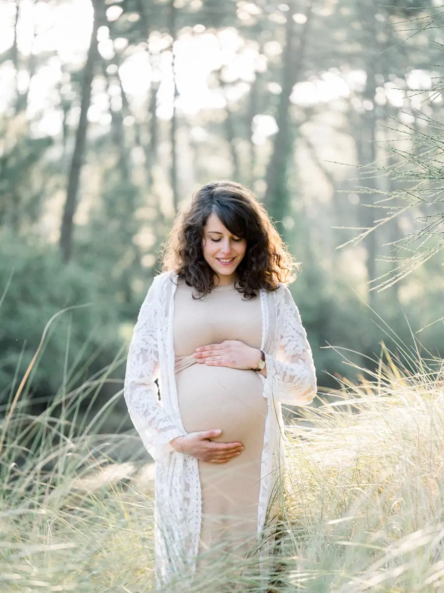 Mother-to-be cradling her bump among tall grasses beneath the pines