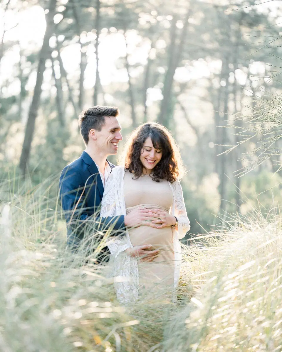 Parents-to-be embracing in tall grasses, hands on the bump