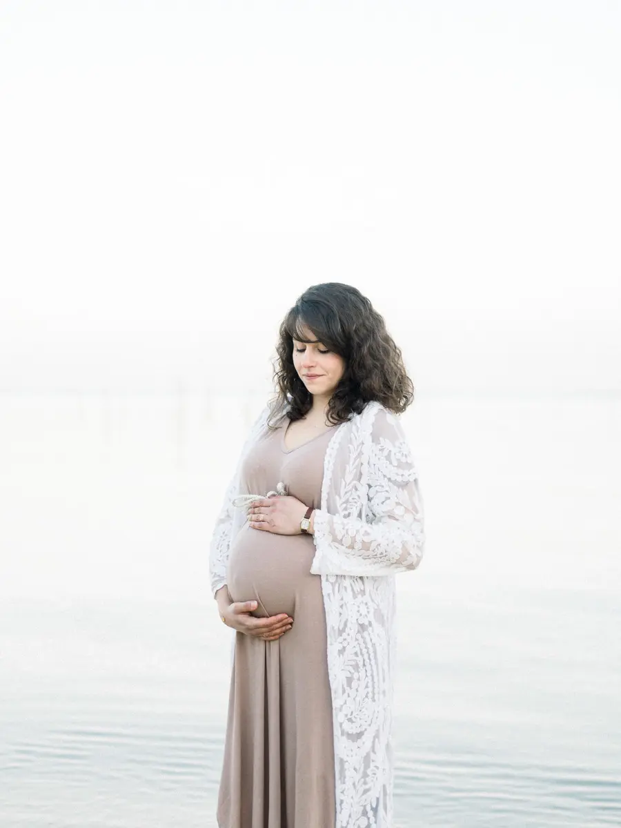 Pregnant woman in a long dress at the water's edge in the mist, at L'Herbe on Arcachon Bay