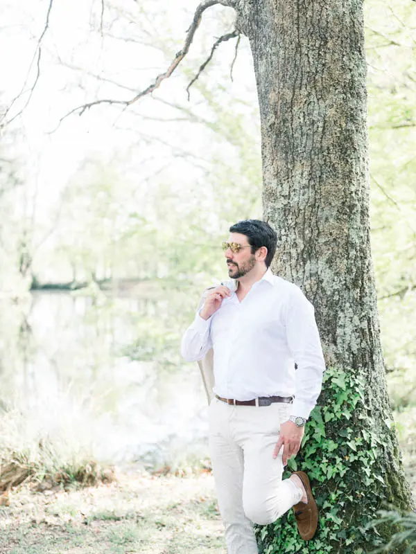 Groom-to-be in a white shirt leaning against an ivy-covered tree