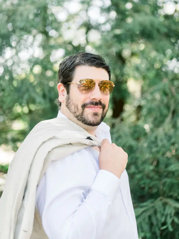 Portrait of the smiling man in sunglasses, jacket slung over his shoulder