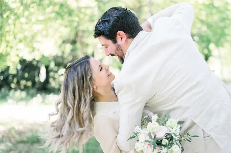 The groom-to-be leaning towards his smiling fiancée, bouquet in hand
