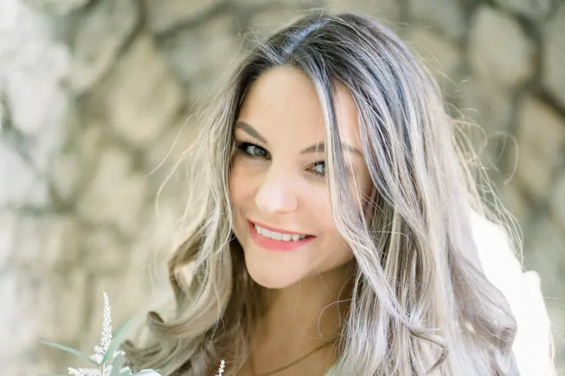 Portrait of the smiling fiancée with long wavy hair against stone