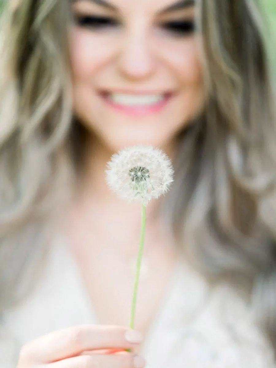 Smiling fiancée holding a dandelion clock, her face softly blurred