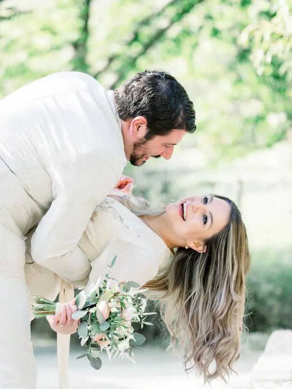 Julien leaning in to kiss a laughing Simone, bouquet in hand