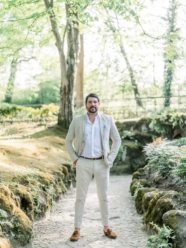 Groom-to-be in a light suit on a path lined with rockwork