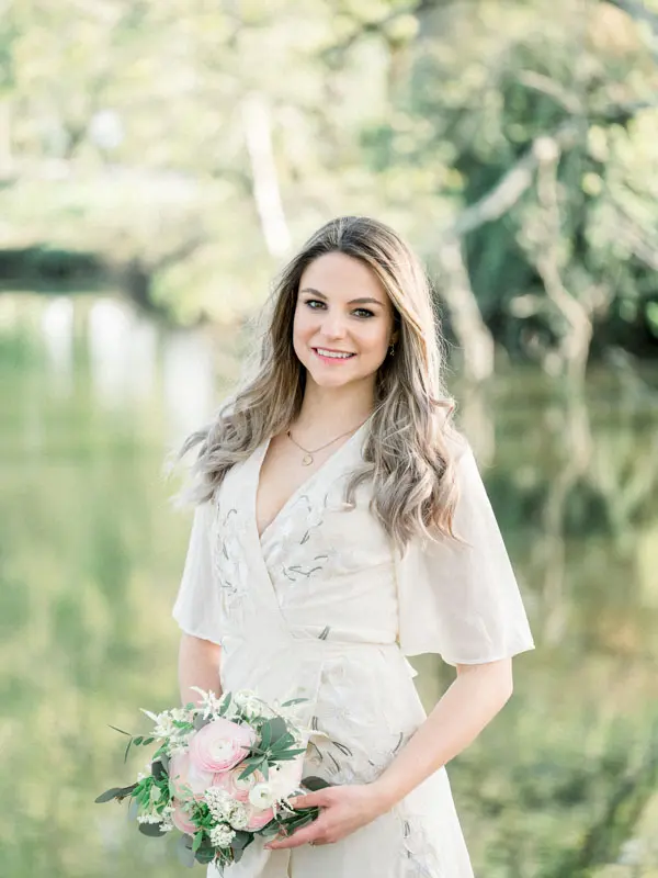 Smiling fiancée by the pond with a pastel flower bouquet