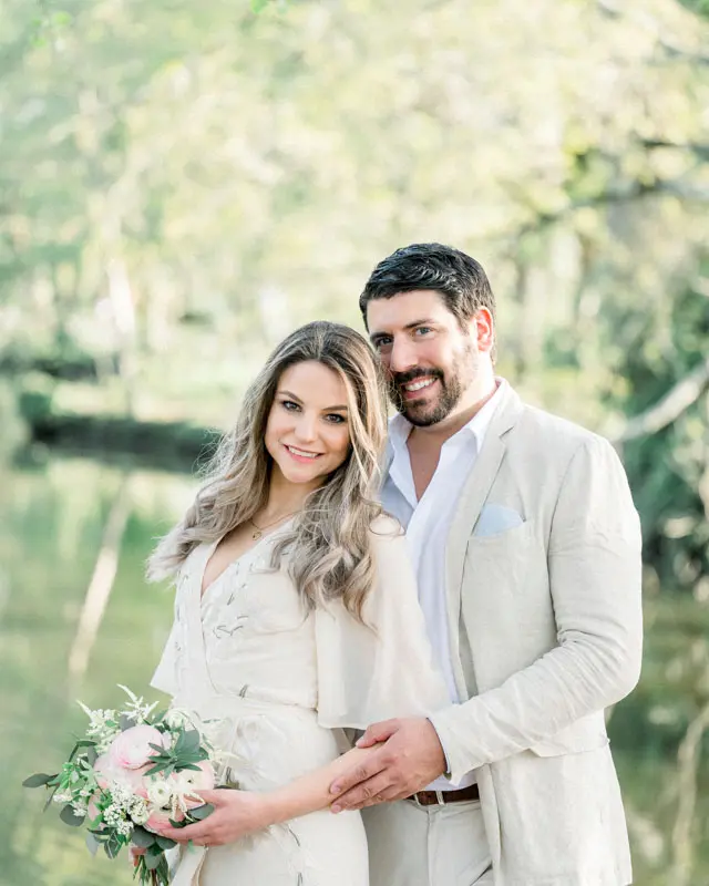 The smiling couple embracing in front of the pond, bouquet in hand