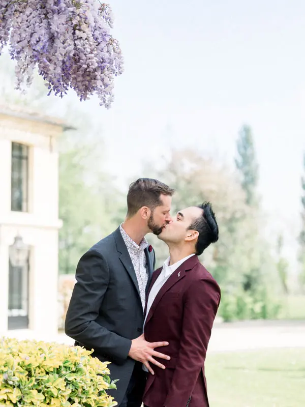 Two men kissing beneath the wisteria at Château Montlabert after a marriage proposal