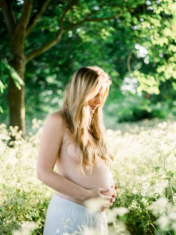 Mother-to-be, bare-chested in a flowering garden, hands on her belly, maternity session
