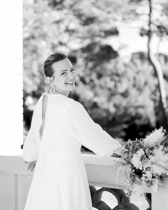 Mariée souriante avec son bouquet sur un balcon, en noir et blanc, à Lanton