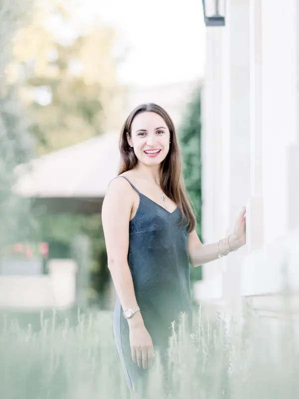 Smiling woman in a blue slip dress leaning on a pale wall at La Grande Maison Bernard Magrez