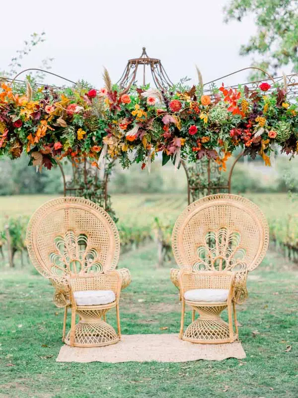 Peacock chairs beneath a floral arch, ceremony at Château de Garde