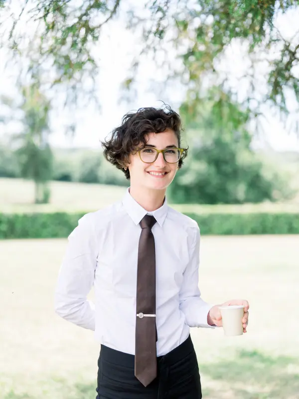 Staff member in a shirt and tie holding a cup in the park of Château de Seguin